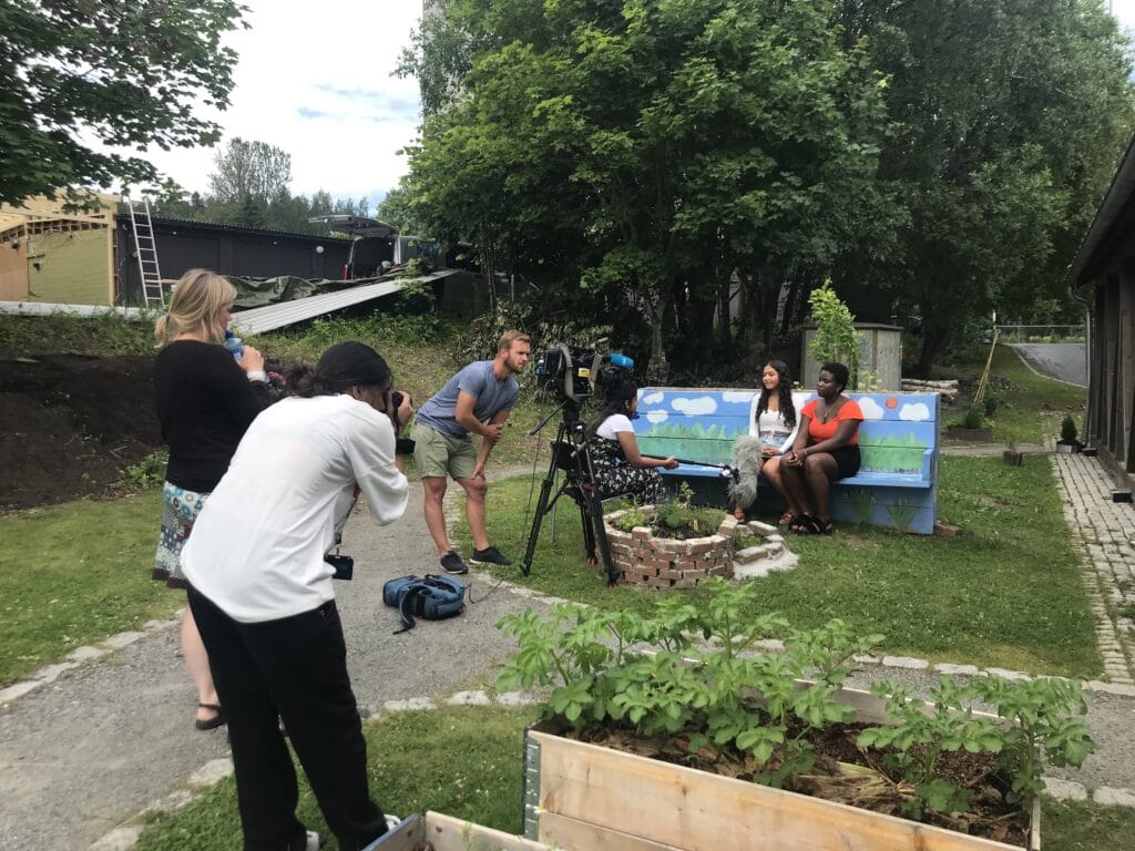 Et team fra NRK Østlandssendingen filmer og intervjuer to unge jenter som sitter på en benk i en park i Groruddalen