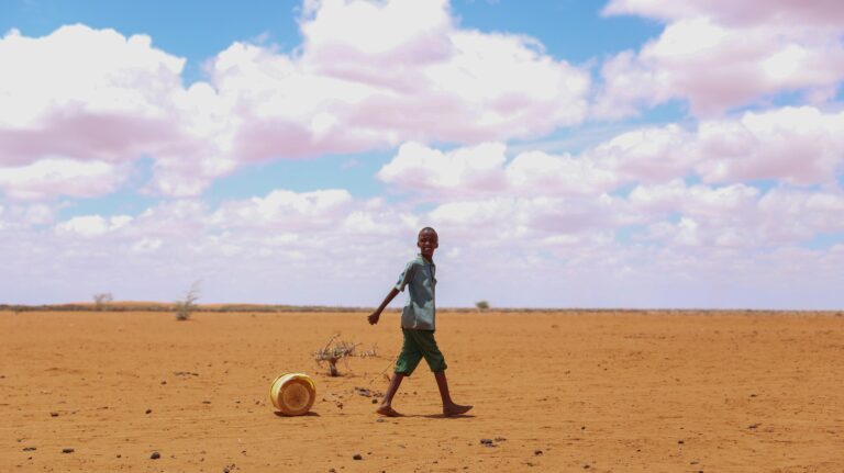En gutt som trekker en vannkanne gjennom et veldig tørt landskap i kenya