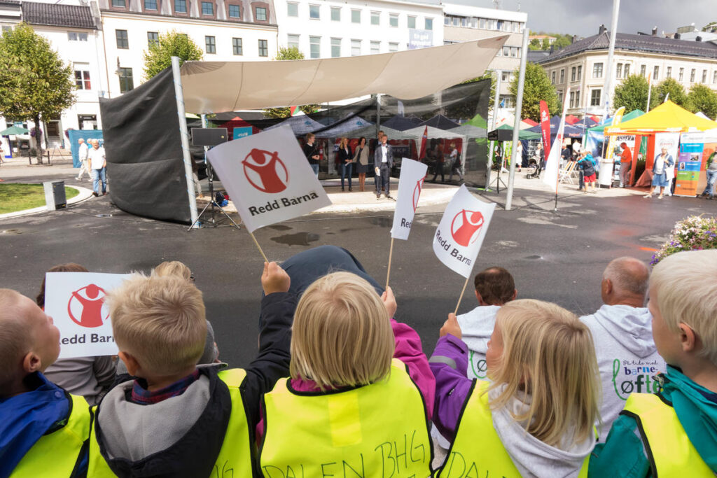 Barn som sitter med Redd Barna-flagg foran en scene på Arendalsuka