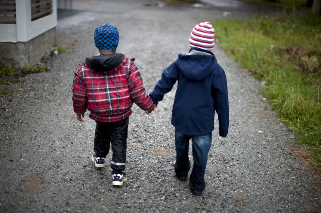 2 barnehagebarn går hånd i hånd med ryggen til kamera. Familiefattigdom er et økende problem i Norge.