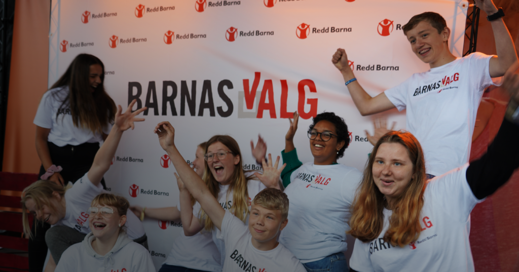 Jublende ungdommer står foran et banner med "Barnas Valg" under liveshow i 2019.