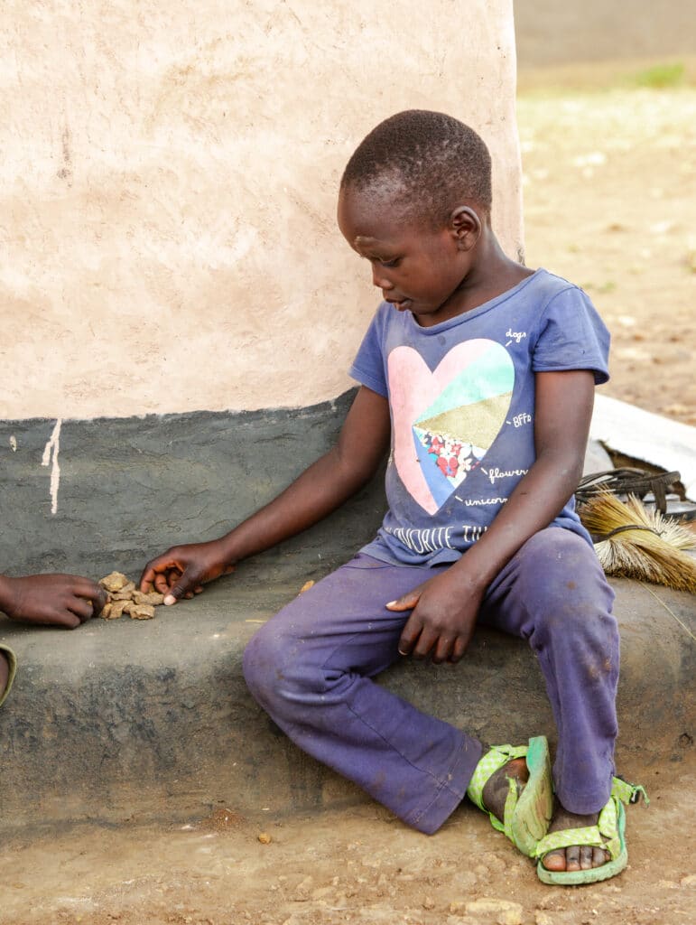 En 6 år gammel gutt sitter utenfor hjemmet sitt i Uganda og teller pinner og steiner. Fra Redd Barnas rapport om utdanning