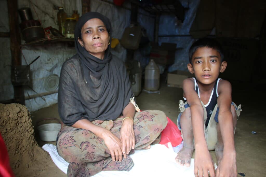En gutt og moren sitter på gulvet i hjemmet sitt i en flyktningeleir i Bangladesh. Området er rammet av oversvømmelser.