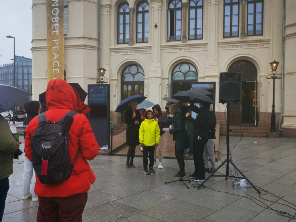 Tolvåringene Abrar og Stella fra Redd Barnas festkomité er klare for sending og utdelingen av Nobels fredspris utenfor Nobelsenteret med regnjakker og paraplyer.