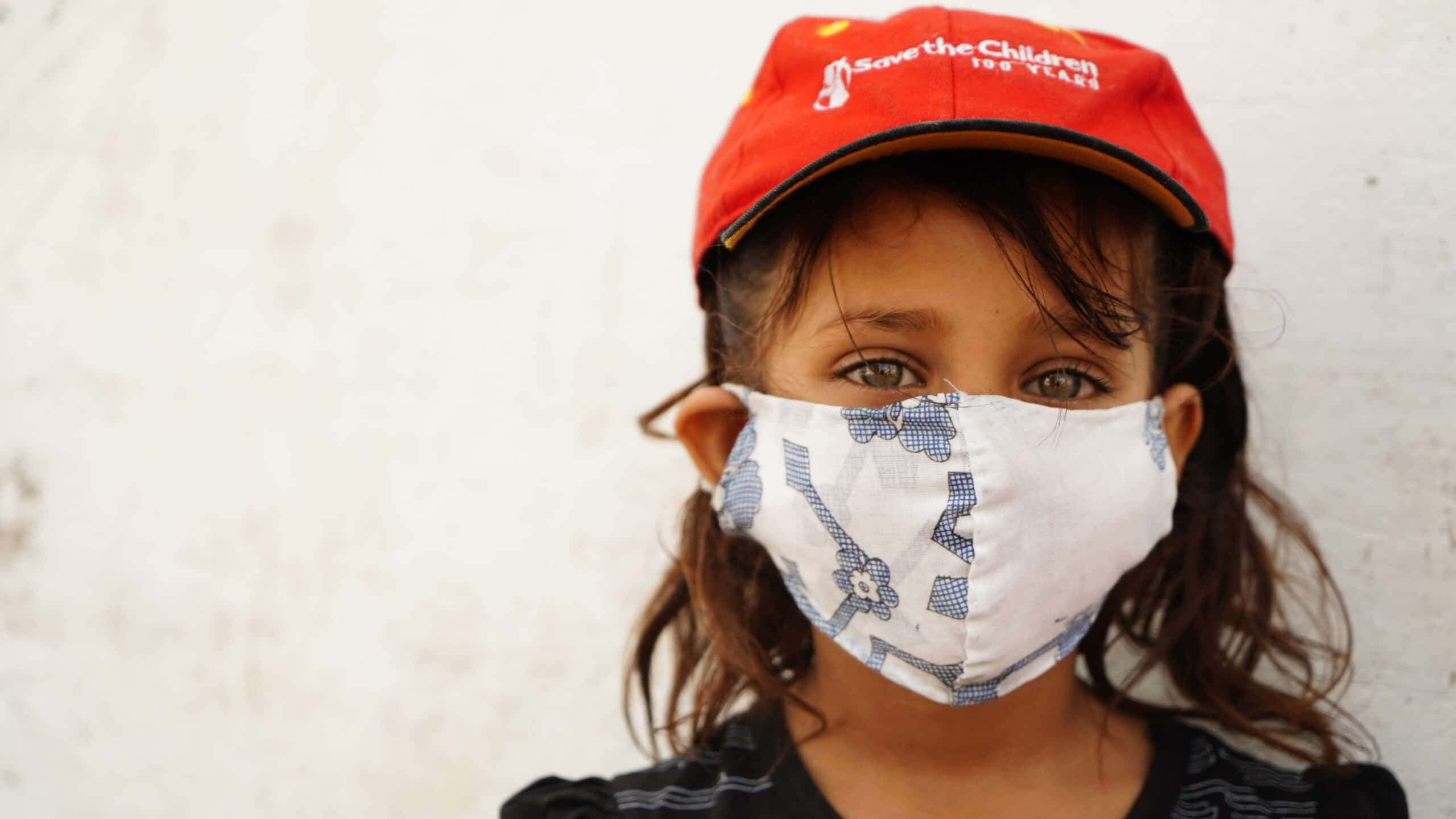 Nærbilde av en jente med ansiktsmaske og rød Redd Barna-cap
