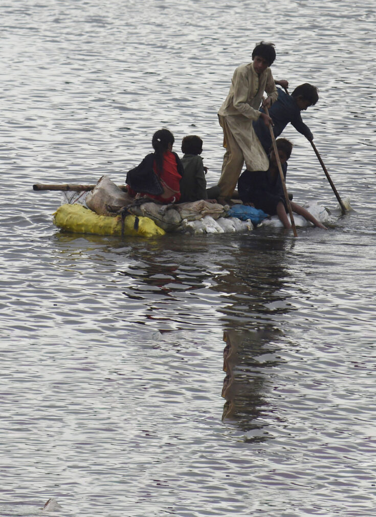 Pakistanske barn på en flåte for å komme seg frem i flomvannet