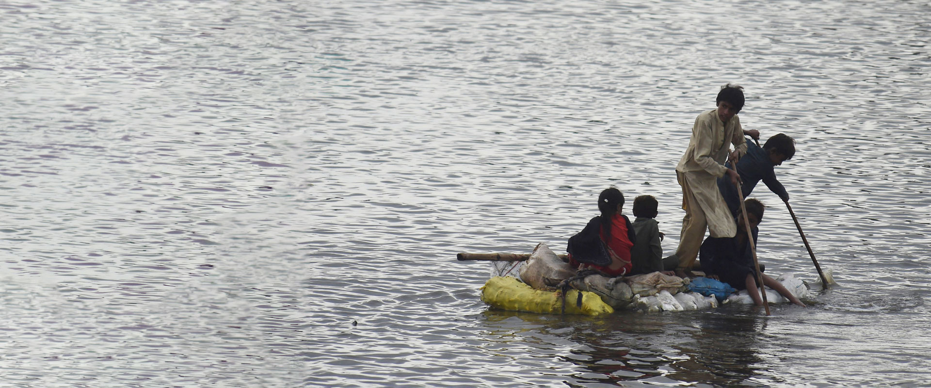 Pakistanske barn på en flåte for å komme seg frem i flomvannet