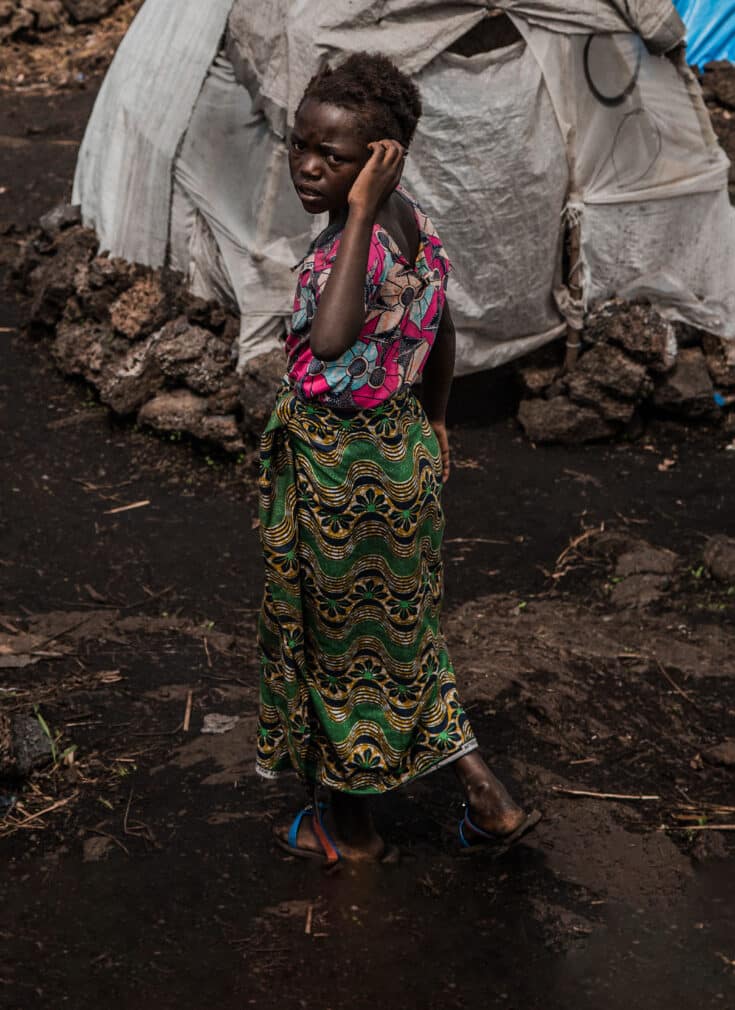 Liliane, en 13 år gammel jente står i fordrivelsesleiren hun og familien måtte dra til på grunn av flom. Hun står ved siden av flere telt og mye gjørme.