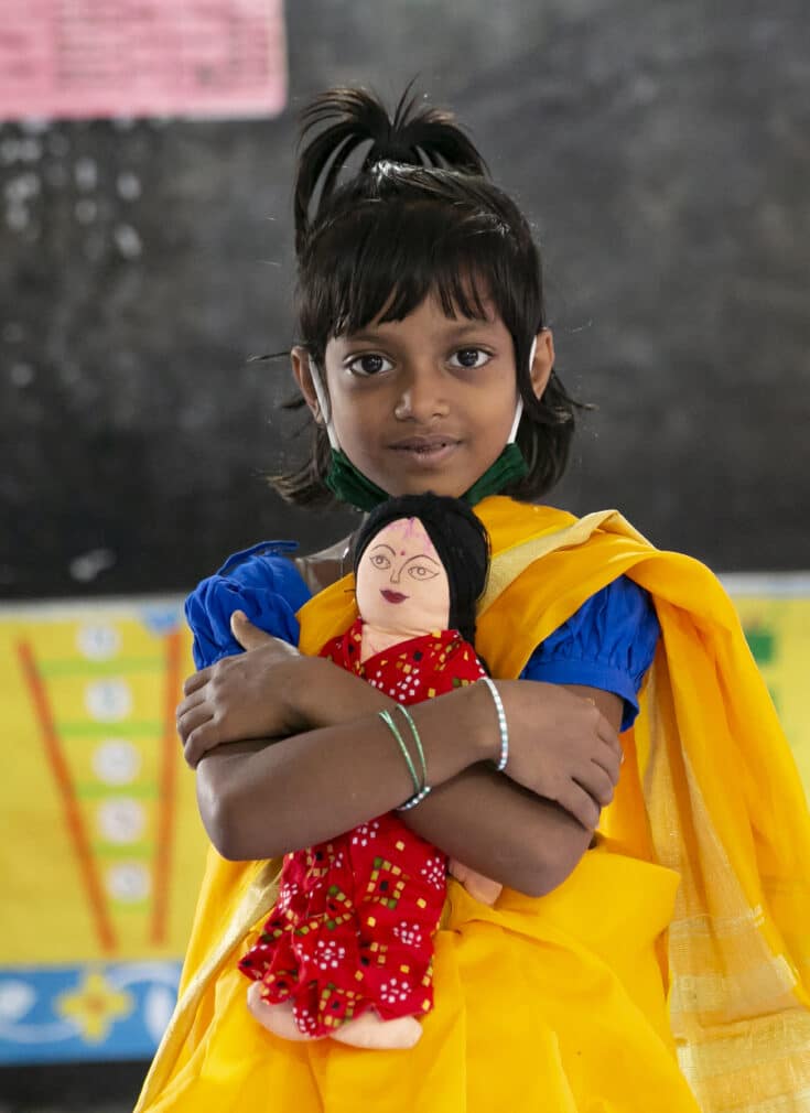 Amina, 6, holding a doll in her classroom