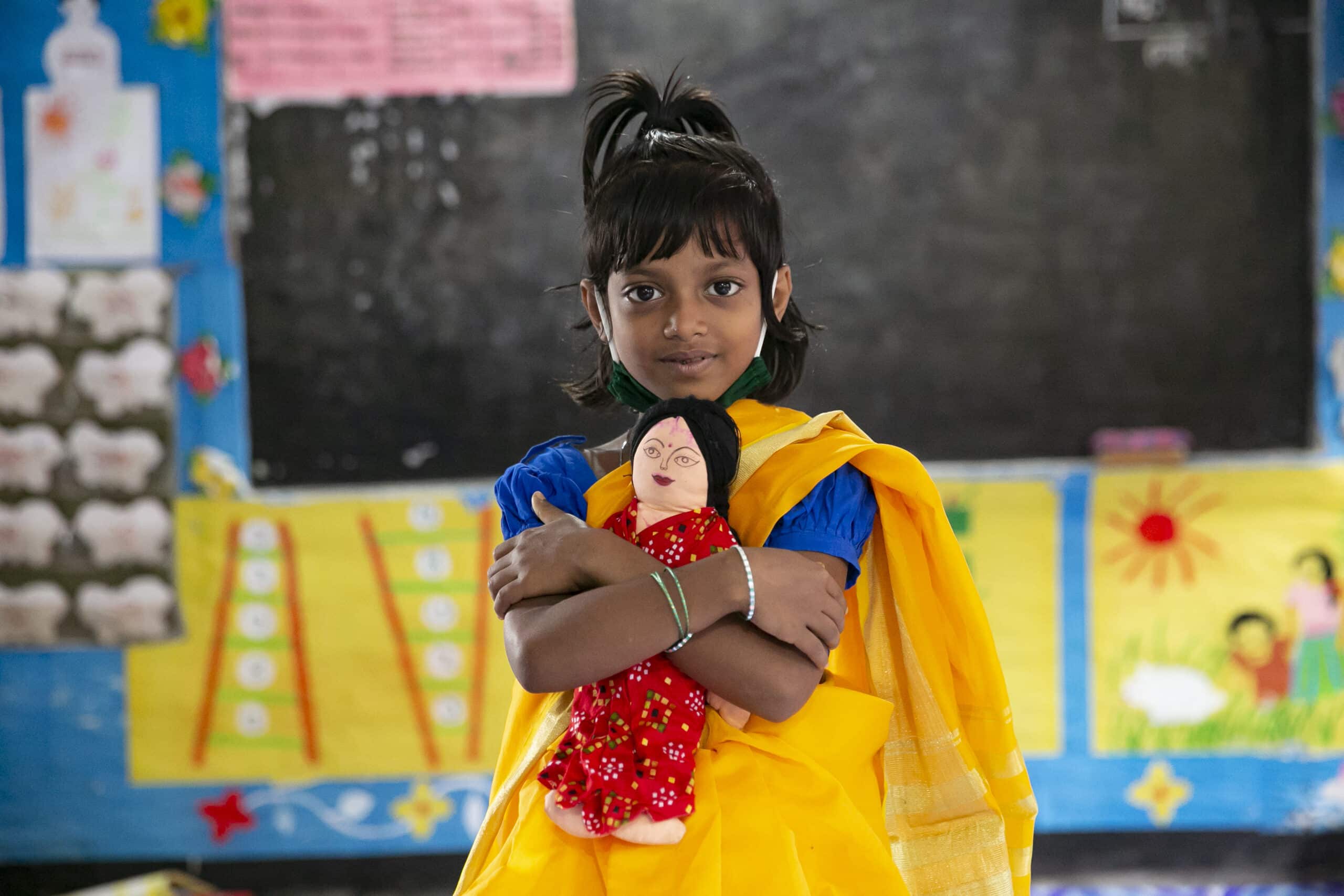 Amina, 6, holding a doll in her classroom