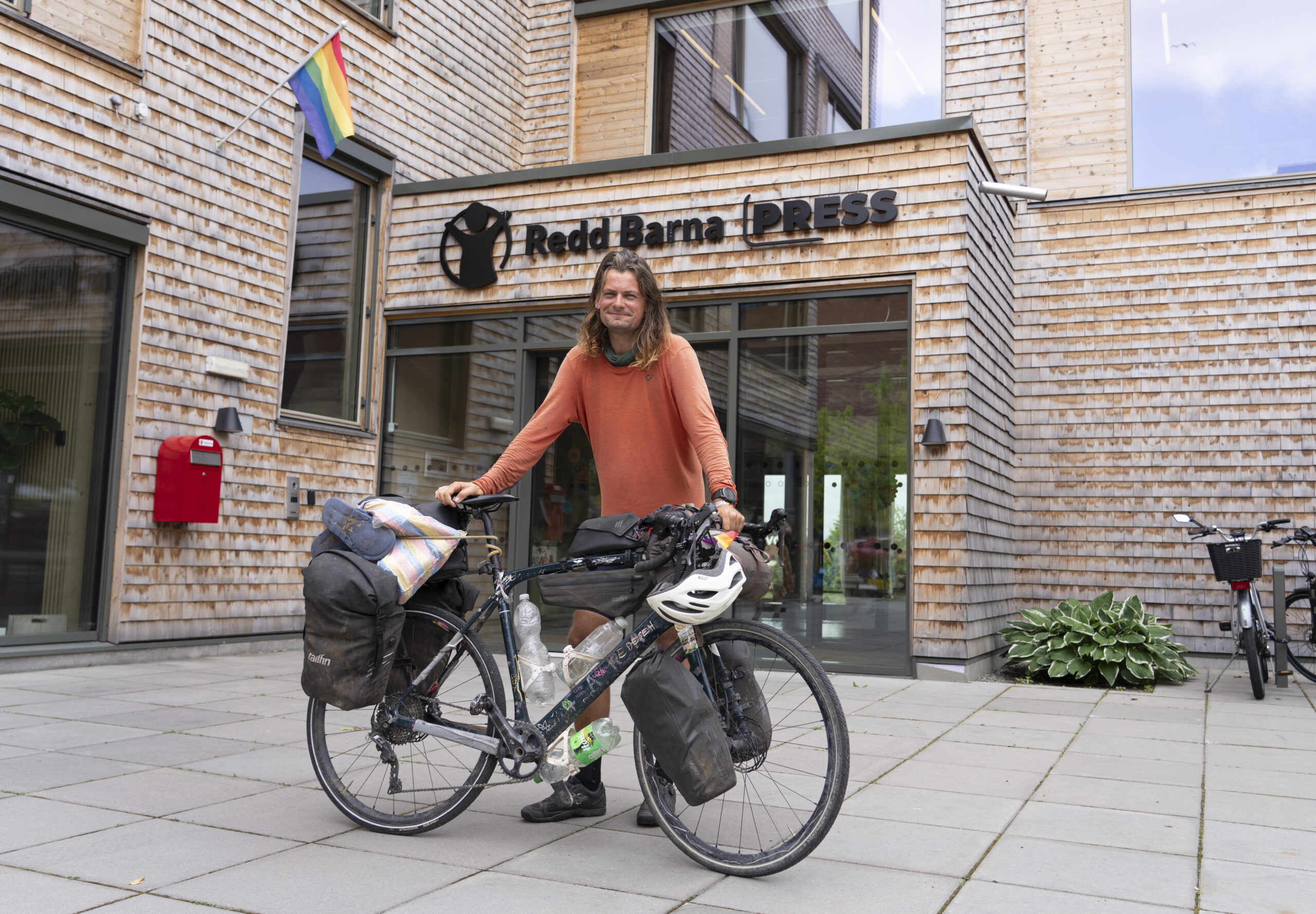 Atle står med sykkelen foran inngangen til Redd Barna-huset. Han har syklet fra Nordkapp til Cape Town og hjem igjen.