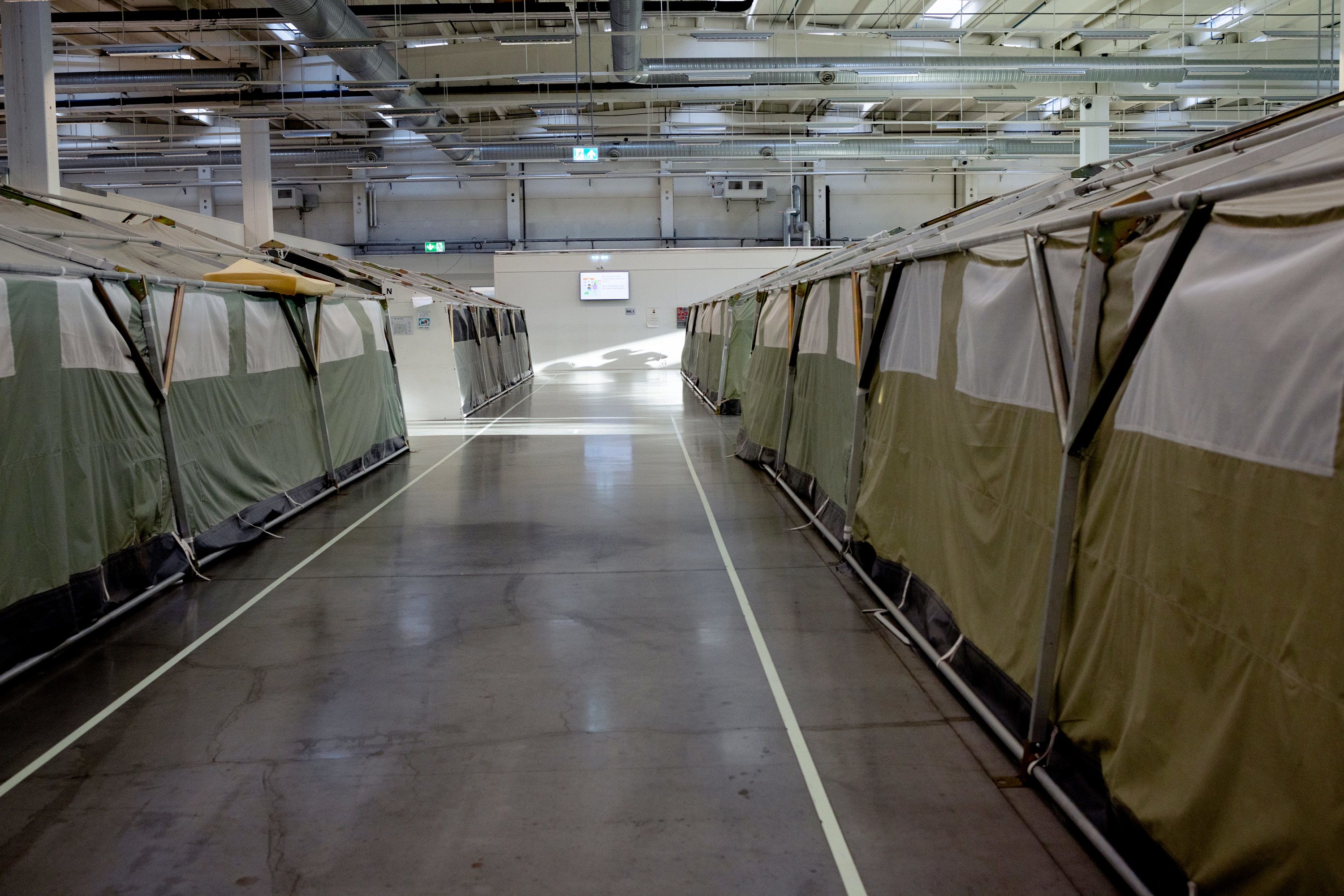 Store grønne og grå telt er plassert på rekke i en stor hall. 