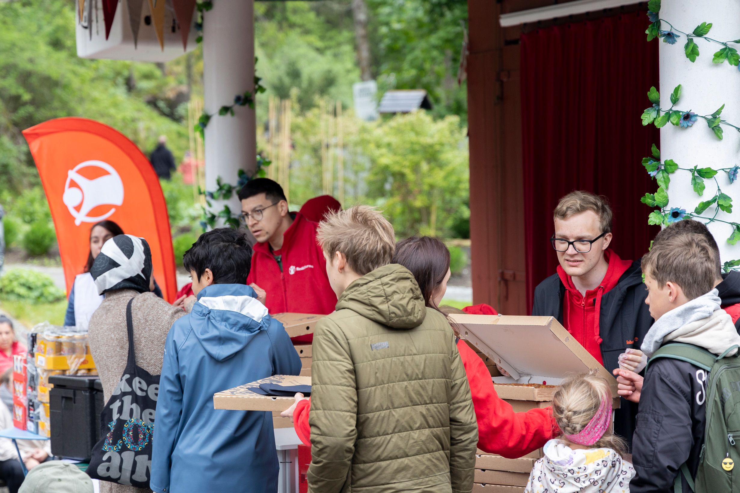 Frivillige fra Redd Barna står bak bordet og deler ut pizza i pizzaesker. 