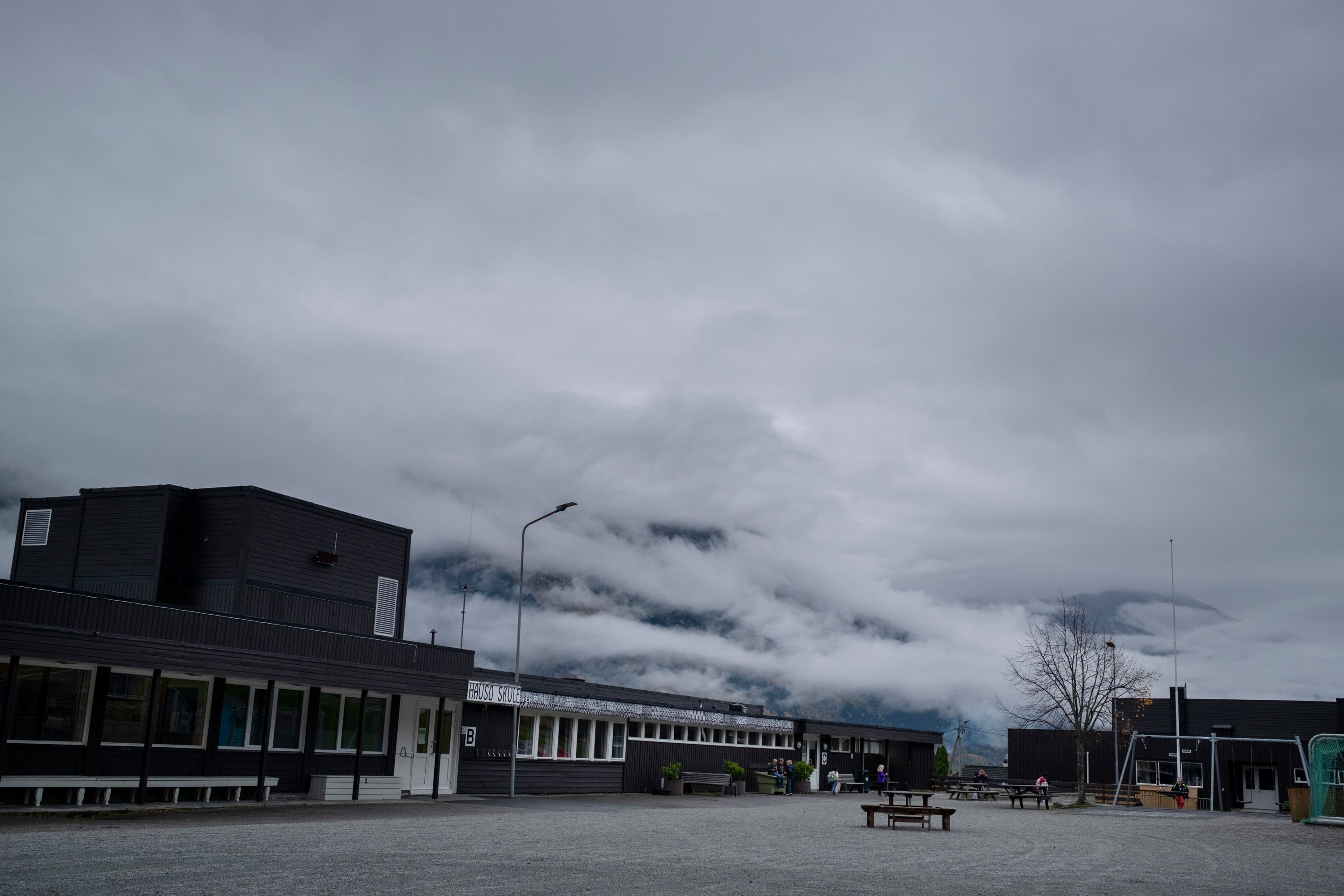 Skolebygget ved Hauso skule foran store fjell dekket av tett tåke.