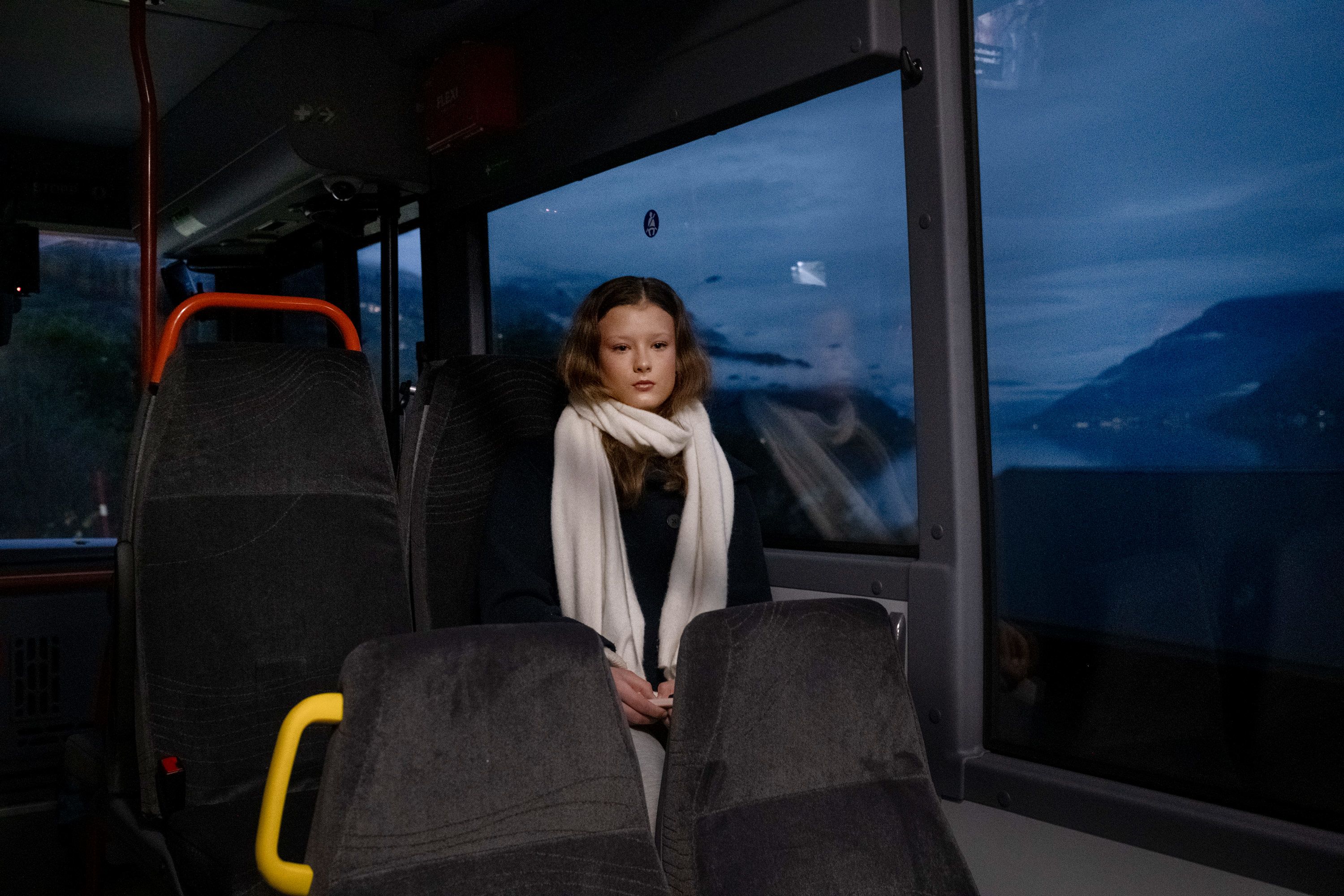 Emma sitter på bussen som kjører langs fjord og fjell.