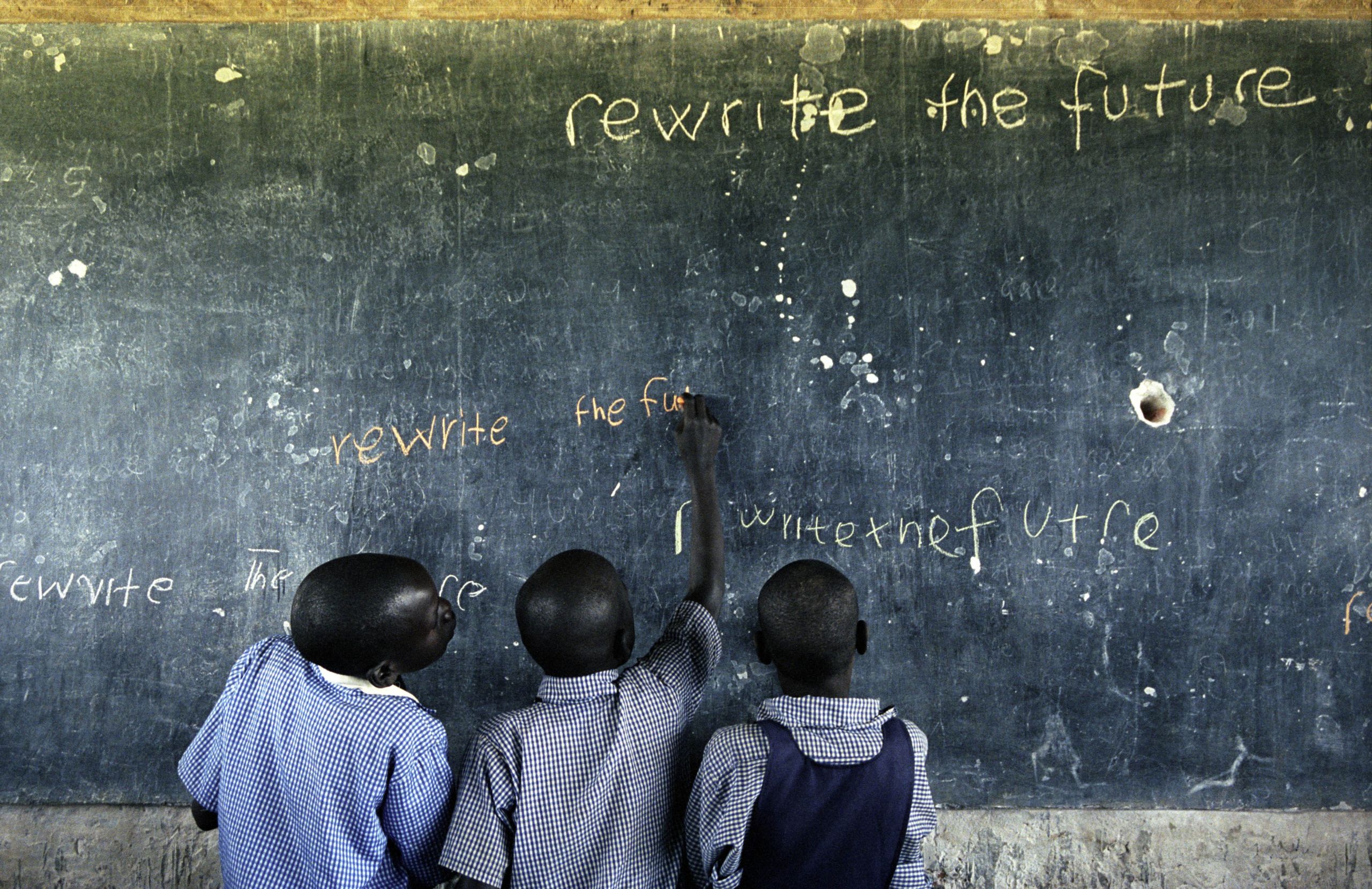 Tre afrikanske gutter skriver på en slitt skoletavle: «rewrite the future».