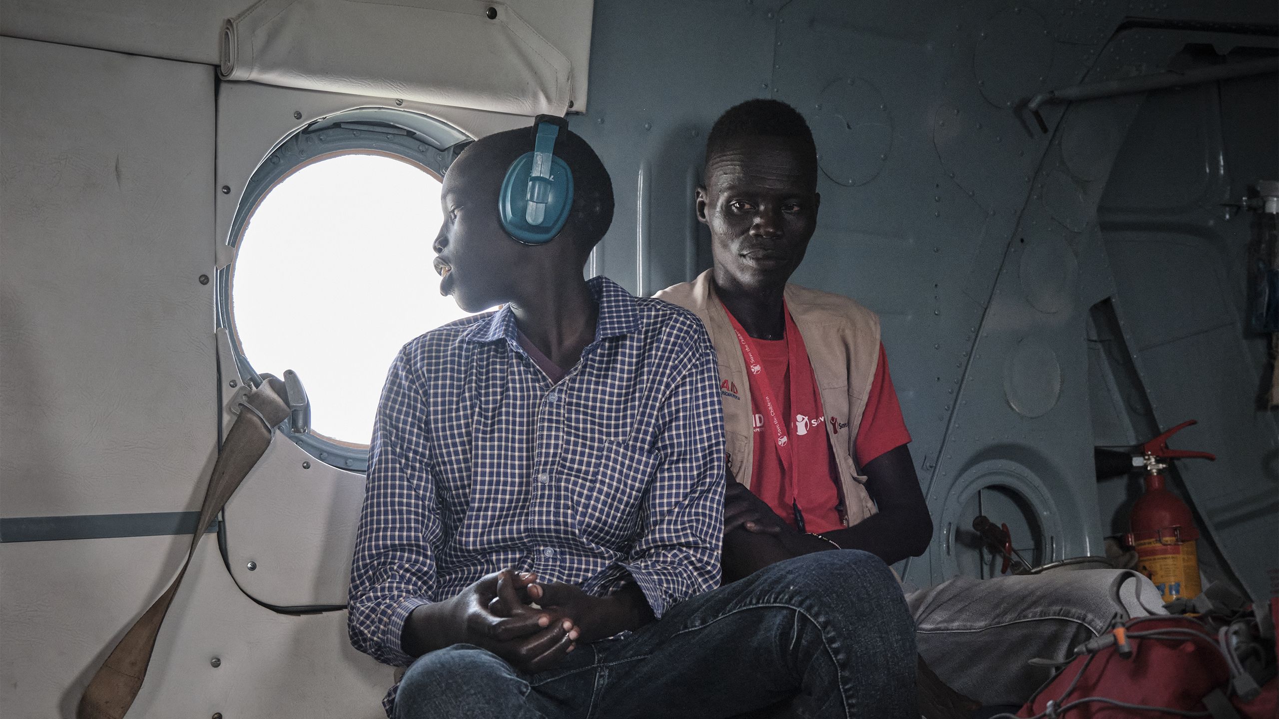Inne i et helikopter sitter gutten med hørselsvern og ser ut av vinduet. Ved siden av ham sitter Redd Barnas feltarbeider.