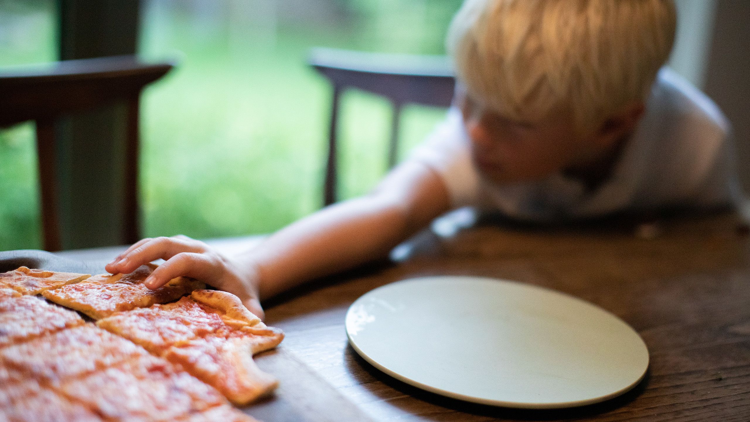 Et barn griper etter et pizzastykke.