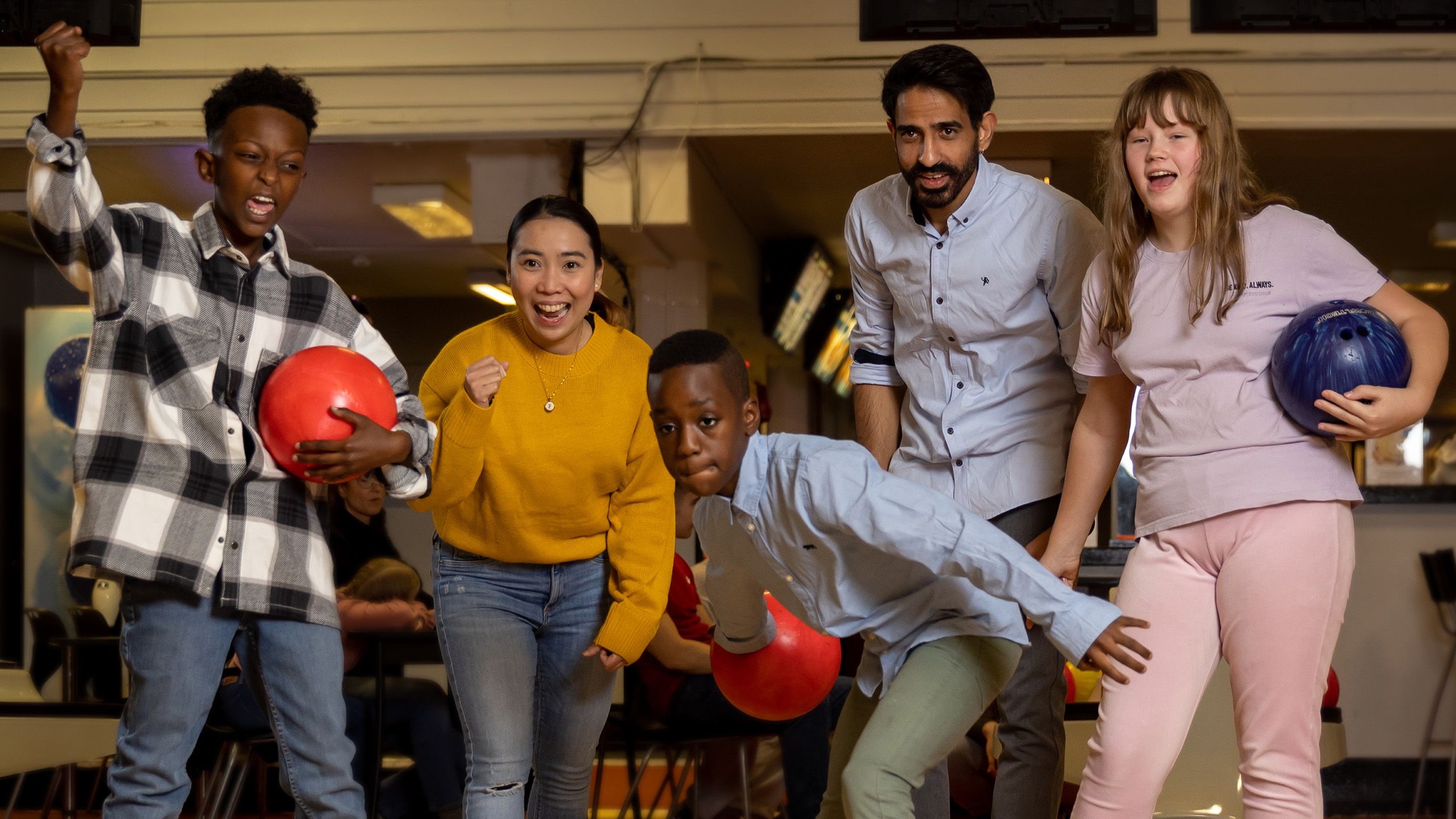Fem unge mennesker på en bowlinghall, noen av dem med bowlingkuler i hendene.